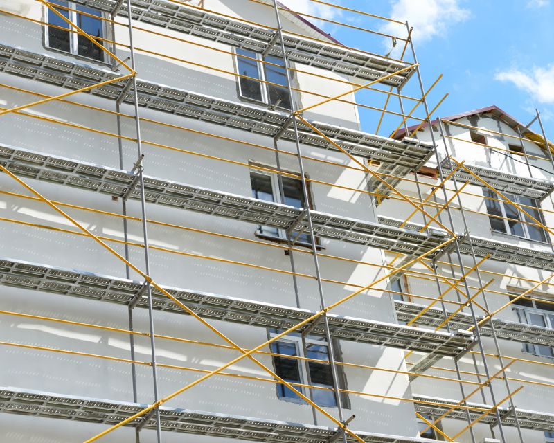 Ein im Bau befindliches mehrstöckiges Gebäude, das mit einem Gerüst bedeckt ist, wobei die Fenster zwischen den Gerüststützen sichtbar sind.