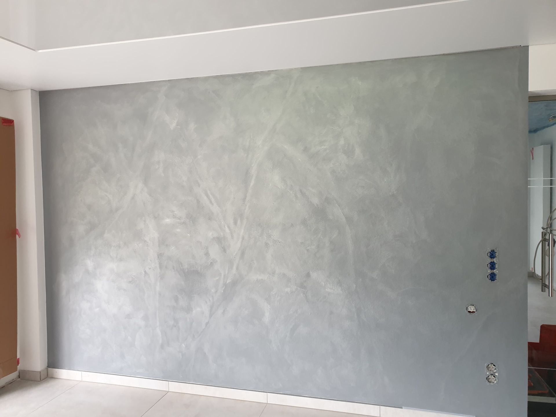 Eine strukturierte graue Wand mit unterschiedlichen Schattierungen, mit Steckdosen auf der rechten Seite und unbearbeiteten Bereichen oben und links.