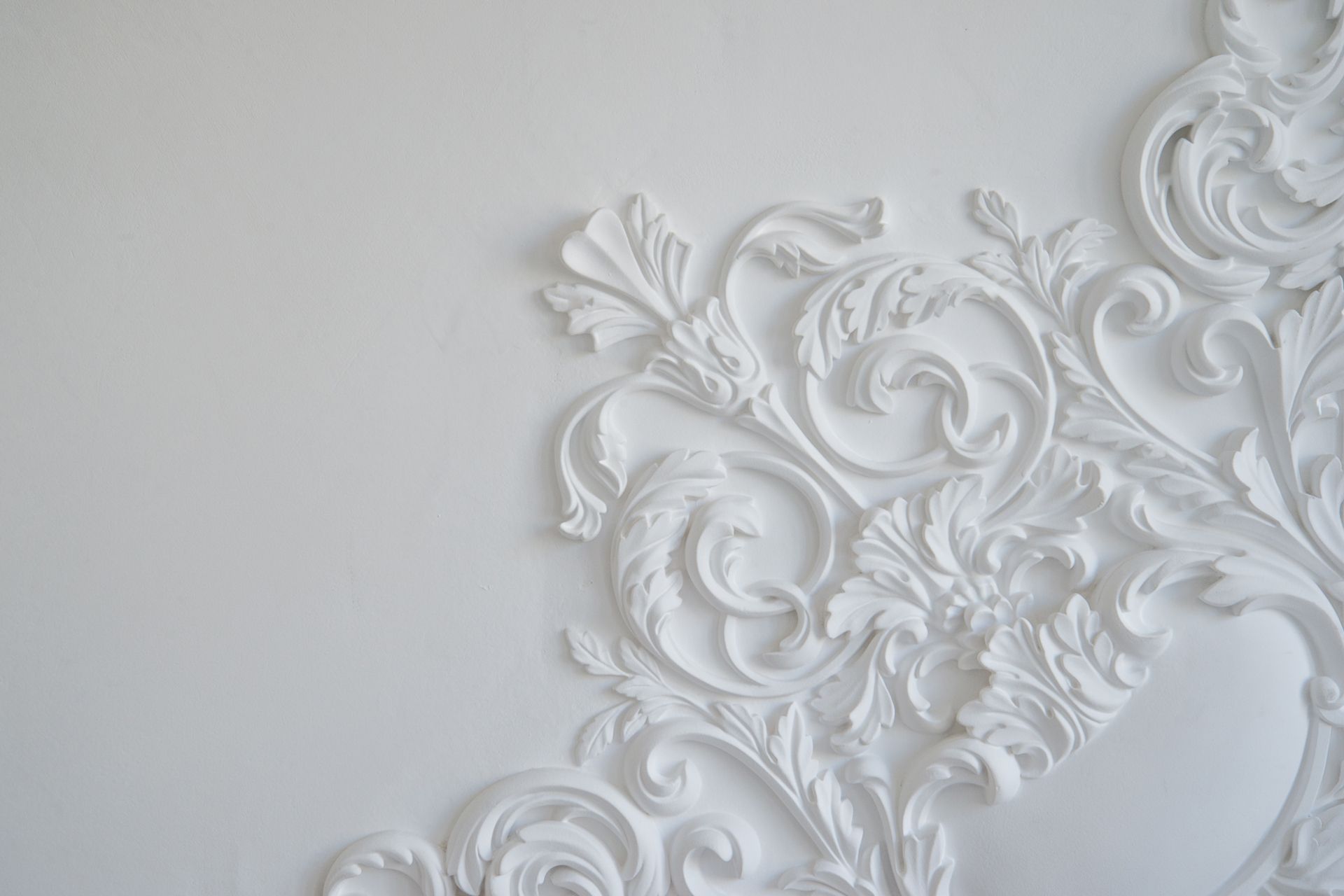 Verziertes weißes Gipsrelief mit komplizierten Blumen- und Schneckenmustern auf einem glatten Hintergrund.